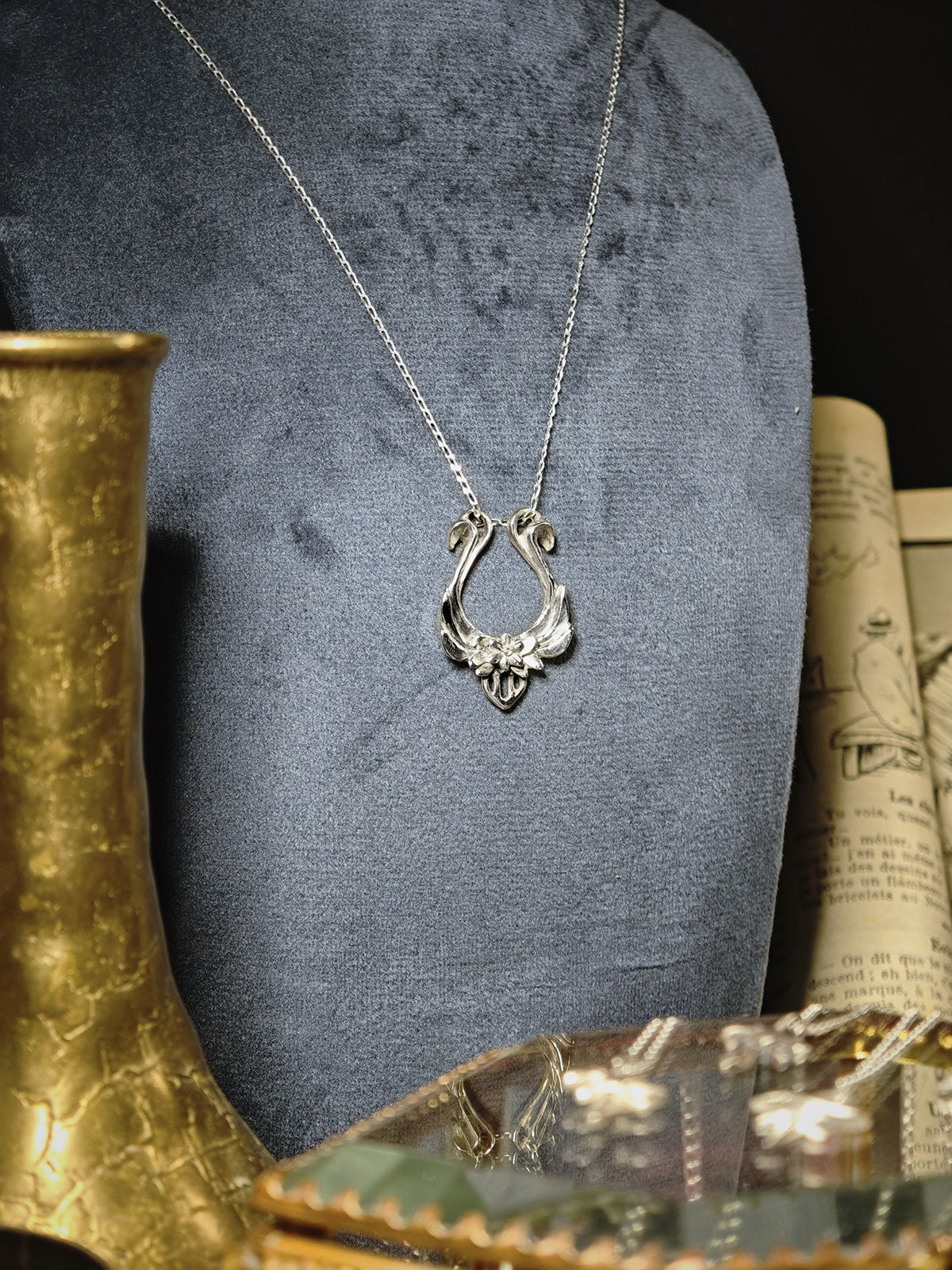 Pendentif lyre d'Orphée en argent 925 sur un buste en velours gris, à côté d'un vase doré